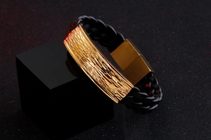 Macro detail of men's braided black leather bracelet with golden hammered metal texture