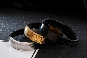 Close-up of men's braided leather bracelets with hammered metal plates in gold, silver, and black