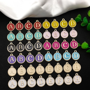 Colorful enamel round letter charms with gold trim arranged on silk for DIY jewelry making