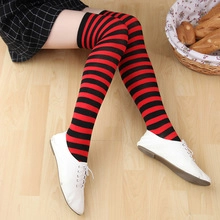 Detail view of black and red striped knee-high socks worn by a model on a wood floor