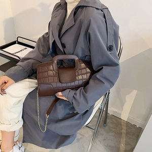 Detail of brown crocodile pattern handbag with silver chain strap and unique top handle