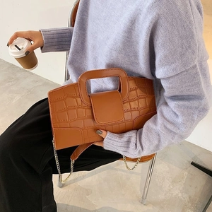 Detail of a brown crocodile pattern leather handbag featuring a stylish metal chain strap