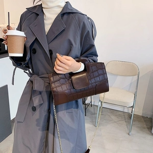 Detail of dark brown crocodile pattern handbag with gold chain strap on grey coat