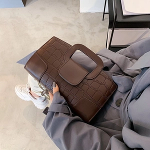 Detail of dark brown crocodile pattern handbag with hollow handle shown in a lifestyle setting