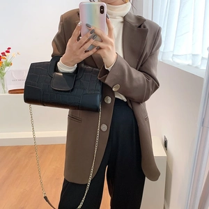 Close-up of black crocodile pattern bag with gold chain strap on a brown blazer