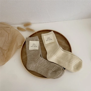Detail of beige and cream thick wool blend socks with woven brand labels on wood