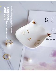 Detail of a white ceramic cat-shaped jewelry tray with golden ears on marble surface
