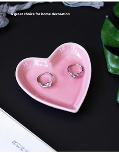 Pink heart-shaped ceramic jewelry tray holding two elegant rings on a black background