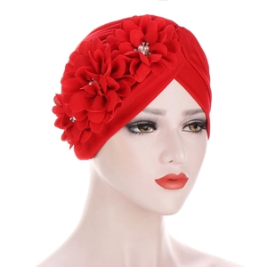 Gros plan sur un turban plissé rouge orné de trois fleurs en tissu et perles