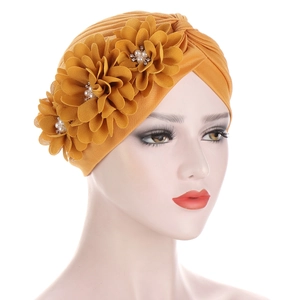 Détail du turban jaune orné de trois fleurs en tissu avec perles et strass brillants