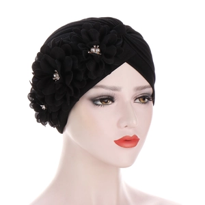Détail d'un turban noir avec trois fleurs 3D, perles et billes dorées sur un mannequin