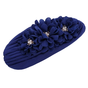 Détail d'un bonnet turban bleu foncé avec trois fleurs décoratives, perles et strass