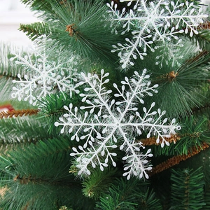 White Christmas snowflake ornament with glitter finish hanging on a green Xmas tree branch