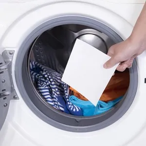 Close-up of white color grabber sheet being placed into washing machine with laundry