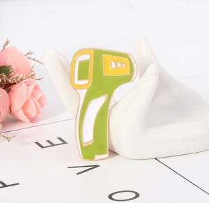 Détail d'une broche émaillée en forme de thermomètre infrarouge vert sur support en céramique