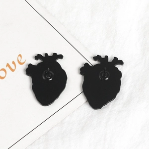 Pair of black anatomical heart pins in gothic alloy style on white fabric background