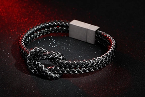 Macro detail of black braided leather bracelet featuring a concentric knot and steel clasp