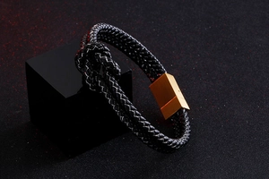 Detail of black braided leather texture and polished gold stainless steel clasp on bracelet