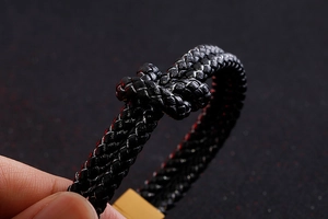 Macro detail of black braided leather bracelet featuring a golden stainless steel knot clasp