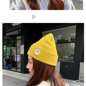 Detail of yellow knit beanie featuring delicate white daisy embroidery on the cuffed brim