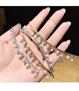 Close-up of hand holding golden and silver rhinestone hair clips with faux pearls