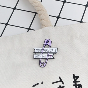 Purple paperclip enamel pin with 'You Are Safe With Me' text on a beige canvas bag