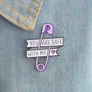 Close-up of purple paperclip enamel pin with You Are Safe With Me text on denim fabric