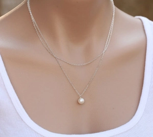Close-up of a double-layered silver necklace with a white pearl pendant on a model