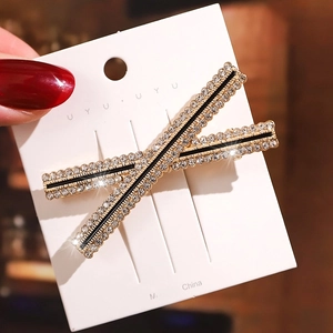 Detail of X-shaped gold hair clip featuring sparkling rhinestones and black enamel accent
