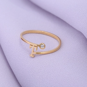Detail van een minimalistische gouden ring met T-vorm en een enkele glanzende steen