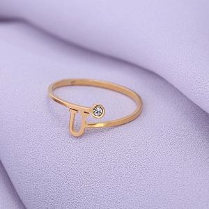 Detail van gouden letter U-ring met een kleine diamant op paarse getextureerde stof