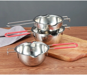 Three stainless steel melting pots with red handles on a wooden board for baking