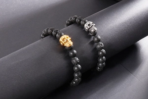 Gros plan de bracelets tête de mort en lave dorée et argentée sur support noir élégant