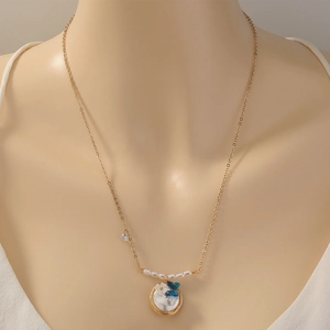 Elegant gold necklace with pearl, blue butterfly, and white flower pendant on a mannequin