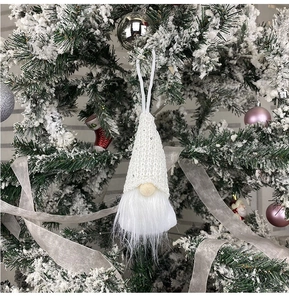 Close-up of a white knitted Christmas gnome ornament hanging on a snowy festive tree