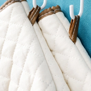 Beige quilted oven mitts with leather loops hanging on a white hook, diamond pattern