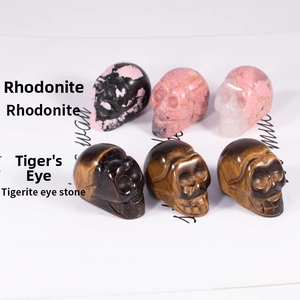 Close-up of hand-carved Rhodonite and Tiger Eye stone skull miniatures in a neat grid display