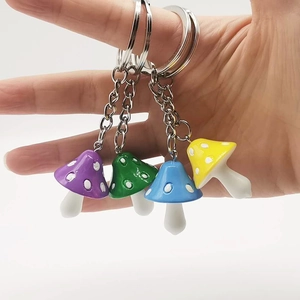 Close-up of four colorful resin mushroom keychains held in hand with metal rings