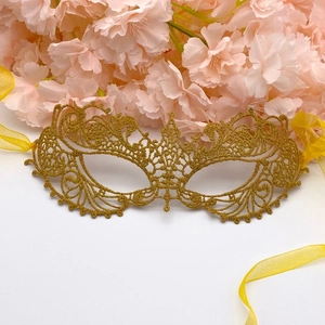Detailed close-up of golden lace phoenix mask with silk ribbons on floral background