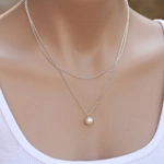 Close-up of double layer silver necklace with round pearl pendant worn by a model