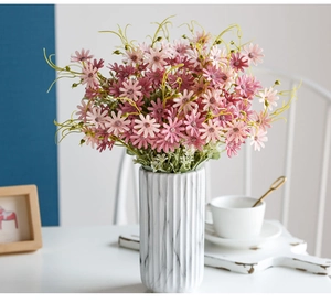 Pink daisy artificial flowers in a white marble vase on a bright wooden table