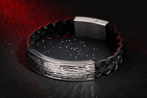 Detail of woven black leather bracelet with hammered stainless steel plate on dark background