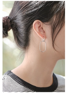 Macro side view of silver geometric oval drop earrings worn by a model