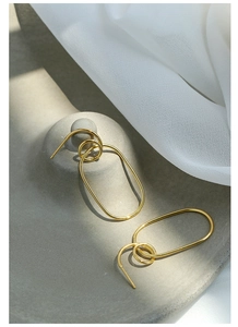 Detailed view of gold geometric intertwined oval earrings with soft lighting and fabric