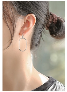 Close-up of long oval silver geometric earrings worn by a model in a minimalist style