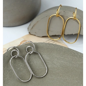 Minimalist gold and silver geometric hoop earrings displayed on a grey stone texture