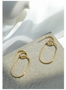 Close-up of geometric gold-plated oval hoop earrings on a grey textured background