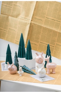 Close-up of ceramic Christmas tree and pink elk figurines on a vintage newspaper background