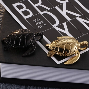 Detail of stainless steel sea turtle pendants in black and gold finishes on a dark book