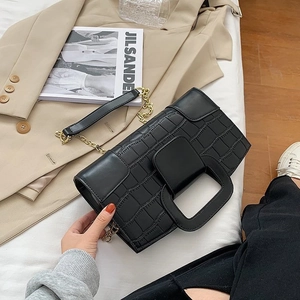 Detail of black crocodile pattern handbag with square handle and golden chain on a bed